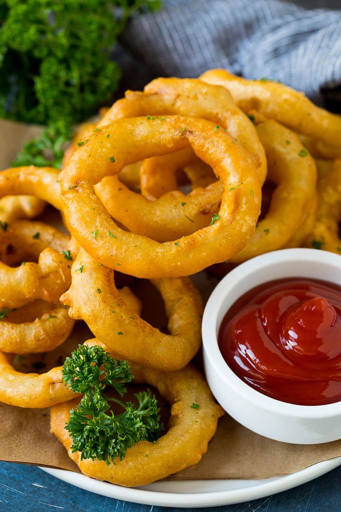 Crispy homemade onion rings that are fried in a flavorful beer batter. #onions #uzhal #appetizer Fried onion rings on a plate with a side of ketchup.