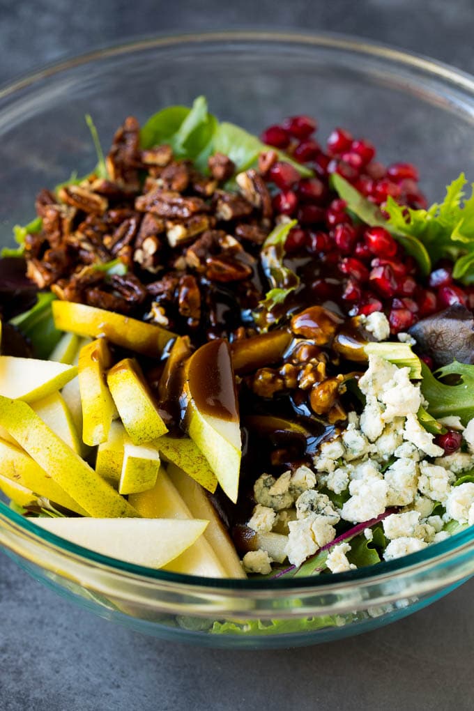 Balsamic dressing poured over a bowl of mixed greens, fruit and pomegranate seeds.