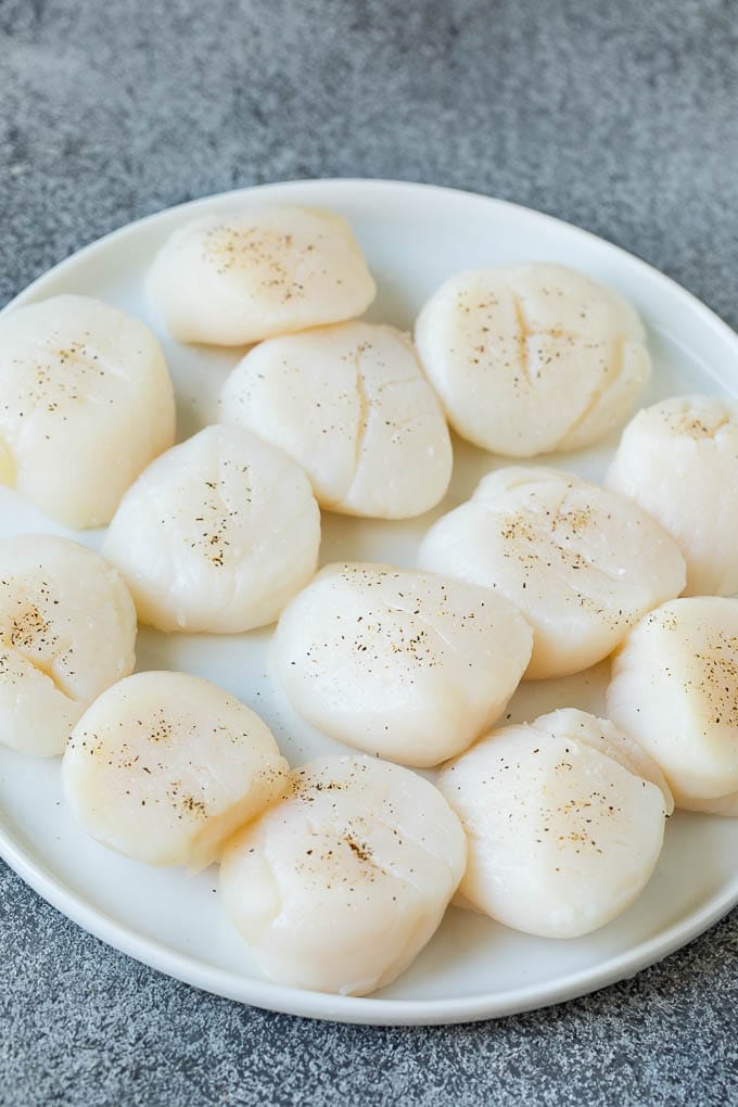 Seared scallops with a garlic and herb butter sauce. An easy and elegant dinner! #seafood #dinner #uzhal Raw sea scallops on a plate.