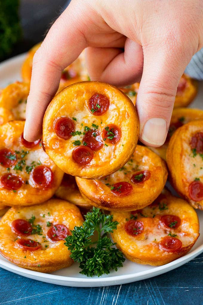 Mini pizzas topped with pepperoni are a fun and easy appetizer option. #pizza #uzhal #appetizer A platter of mini pizzas with a hand reaching for one.
