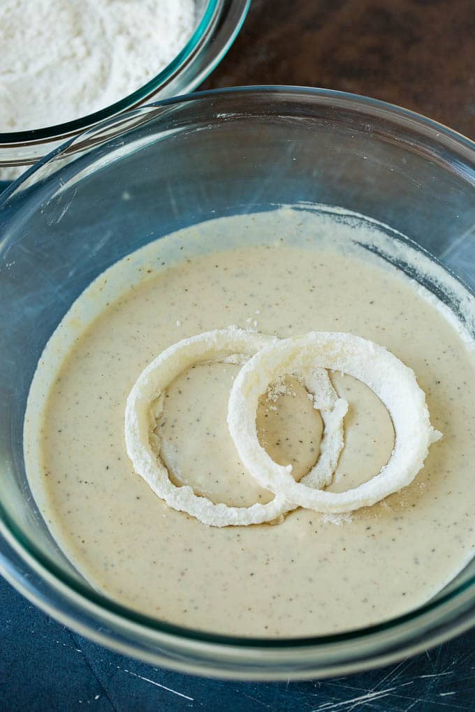 Crispy homemade onion rings that are fried in a flavorful beer batter. #onions #uzhal #appetizer Floured onions in a bowl of beer batter.