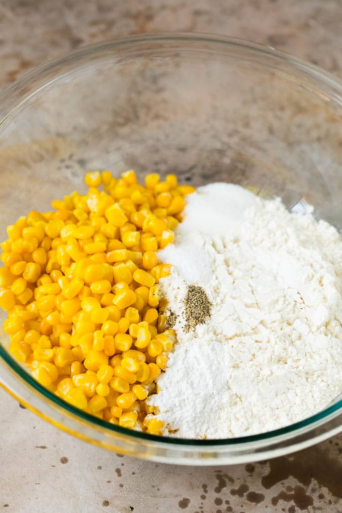 These crispy corn fritters are easy to make and are the perfect appetizer or lighter main course. #corn #uzhal Flour, corn and seasonings in a mixing bowl.