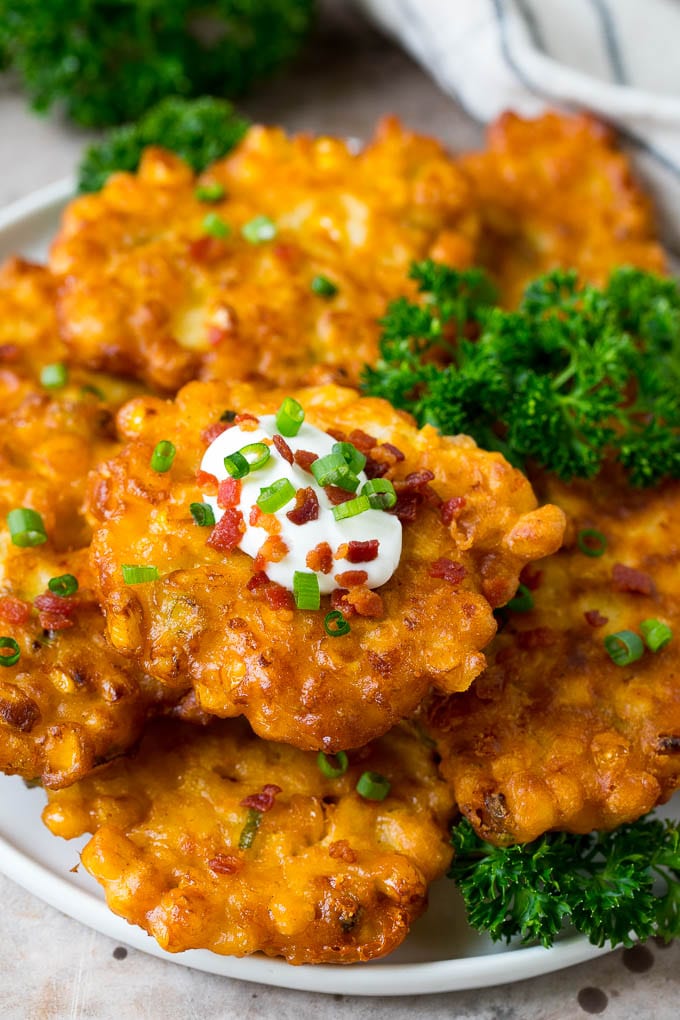 These crispy corn fritters are easy to make and are the perfect appetizer or lighter main course. #corn #uzhal A plate of corn fritters garnished with parsley, and topped with sour cream.