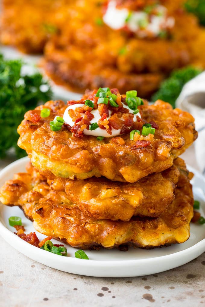These crispy corn fritters are easy to make and are the perfect appetizer or lighter main course. #corn #uzhal A stack of corn fritters topped with bacon, sour cream and green onions.