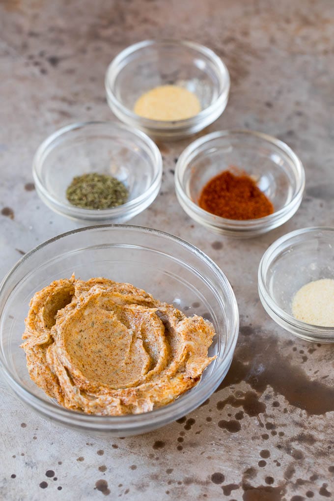 Butter mixed with herbs and spices along with bowls of seasonings.