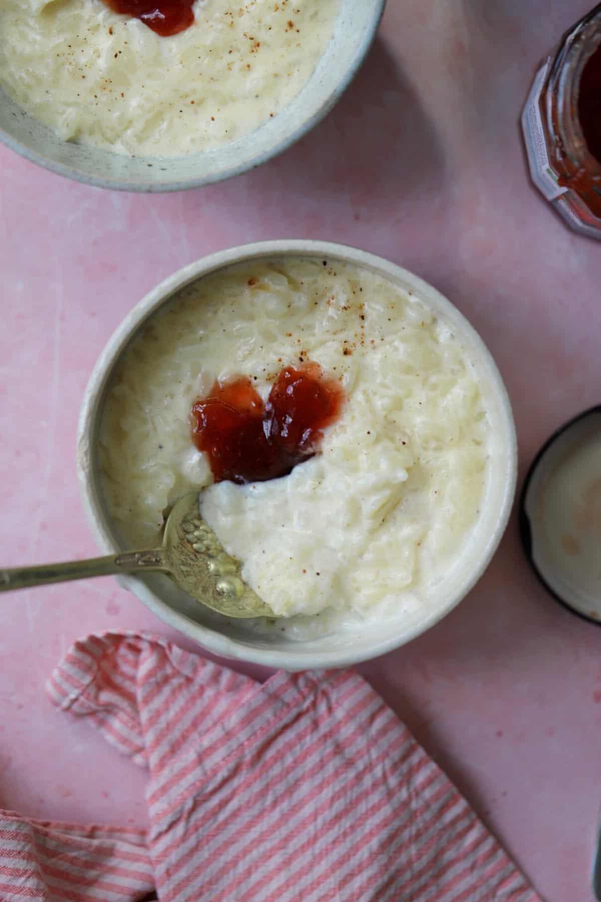 Una ciotola di budino di riso in slow cooker con marmellata sopra e un cucchiaio.
