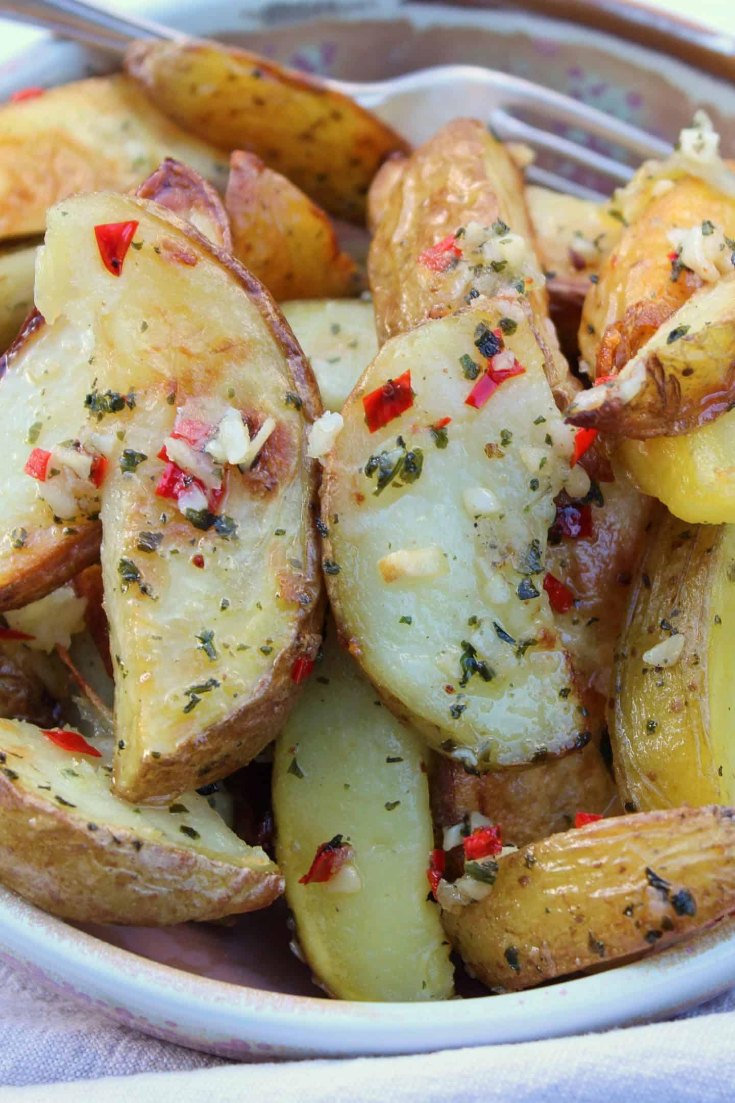 Patate a spicchi senza glutine 2 Una ciotola di spicchi di patate senza glutine con aglio e peperoncino.