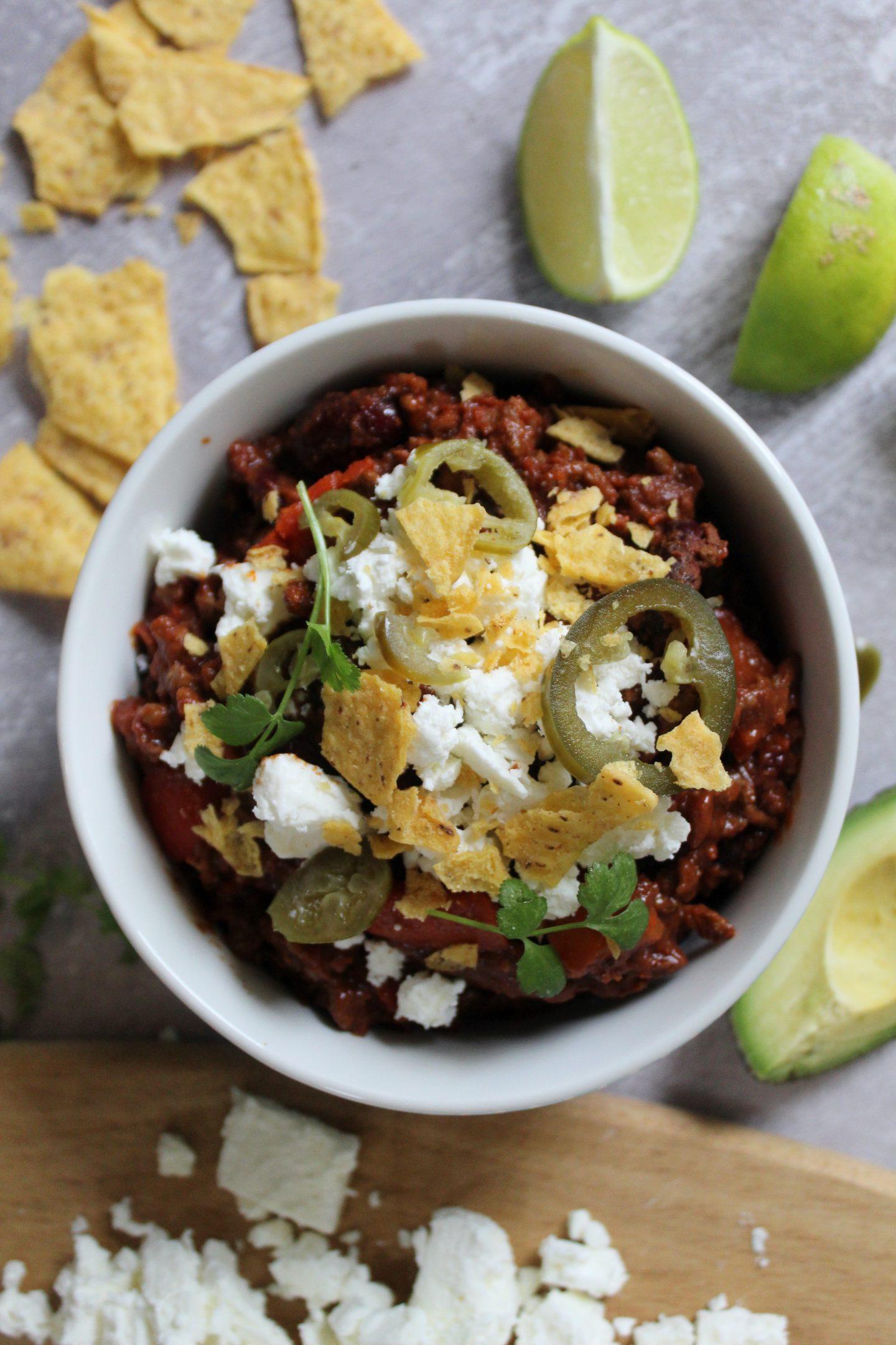 Chilli Con Carne Senza Glutine 3 Una ciotola di chilli con carne guarnita con nachos, feta e jalapeños.