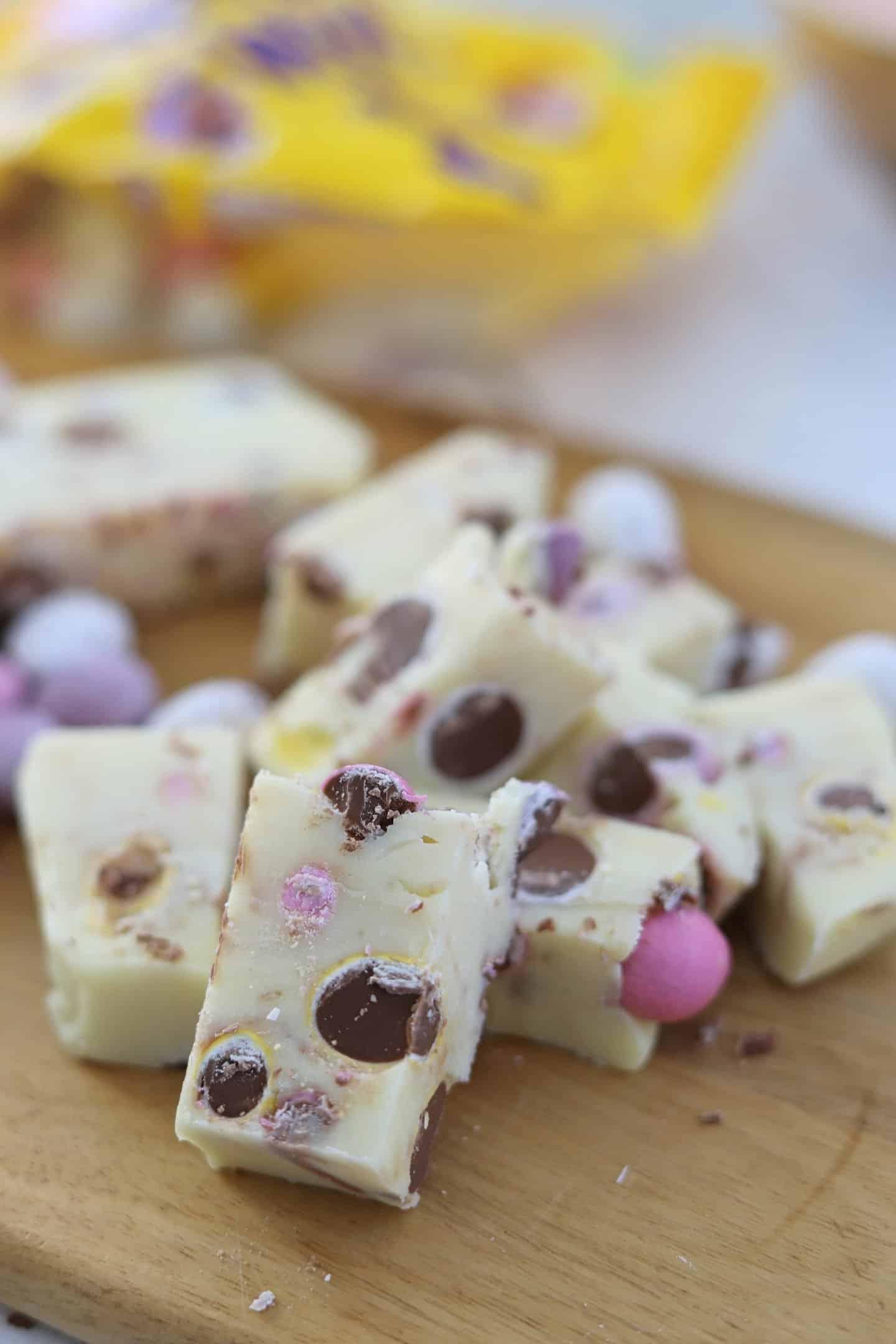 Fudge alle Mini Uova 3 Cubetti di fudge con mini uova su un tagliere di legno.