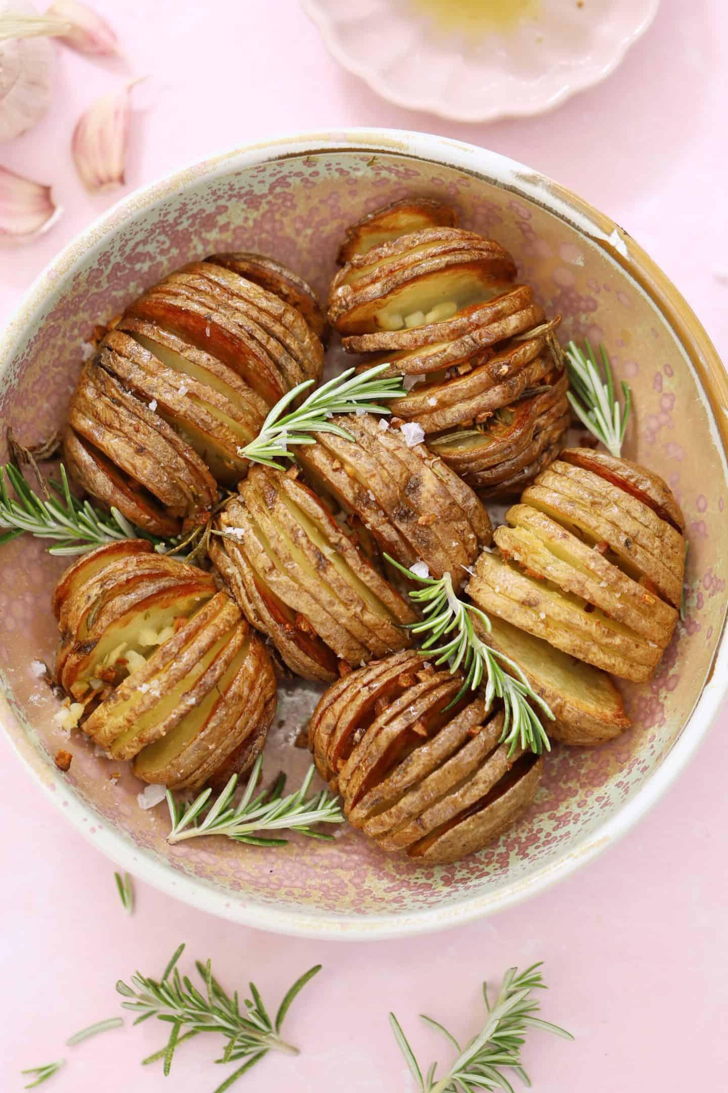 Patate Hasselback in friggitrice ad aria 2 Una ciotola di patate hasselback cotte in friggitrice ad aria con rametti di rosmarino.