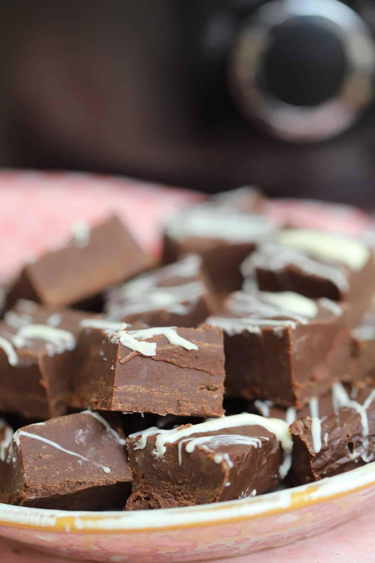 Fudge al Cioccolato in Slow Cooker 4 Un mucchietto di fudge al cioccolato davanti a una slow cooker su un piatto rosa.