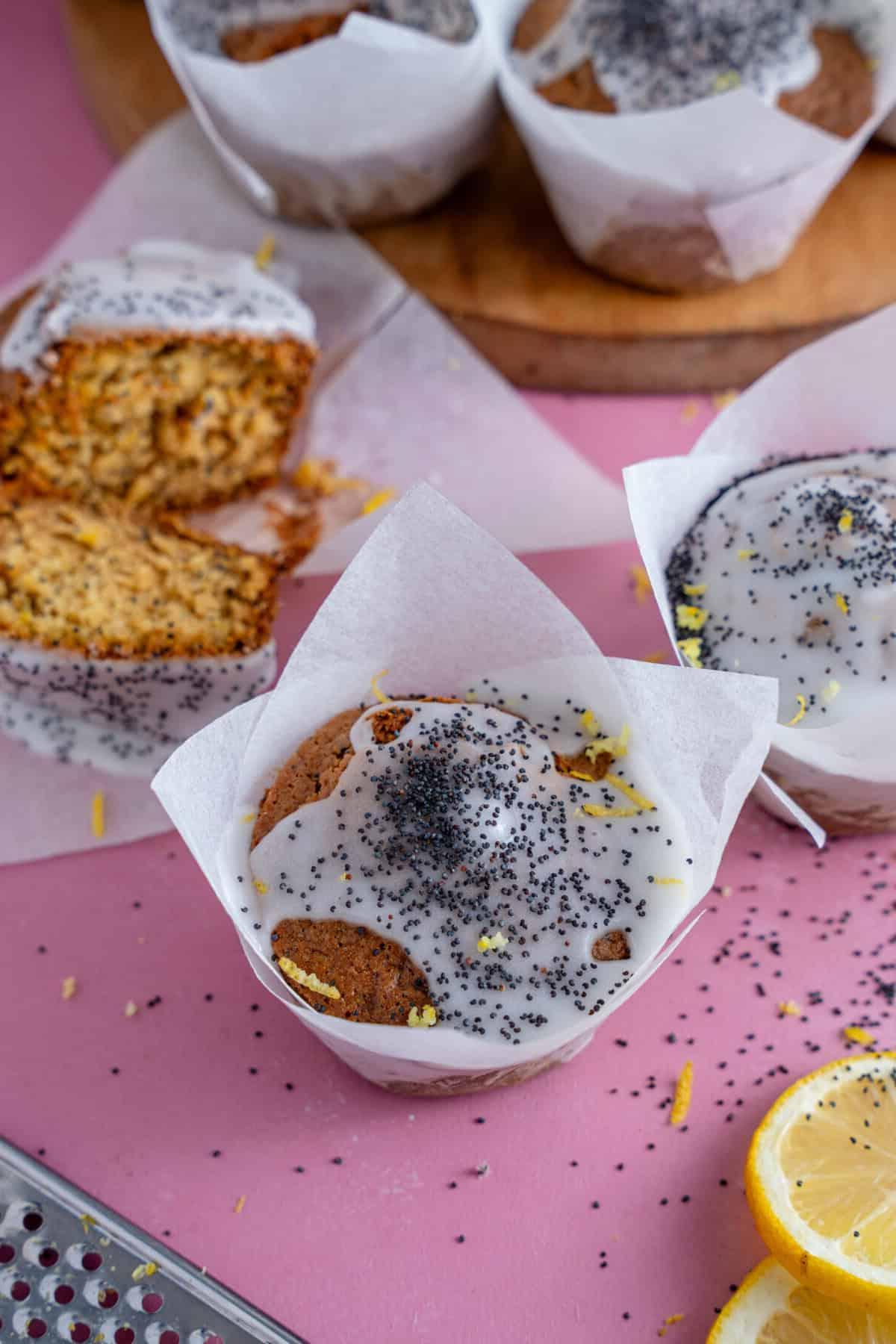 Muffin al limone e semi di papavero su un piano di lavoro rosa con uno tagliato a metà sullo sfondo.