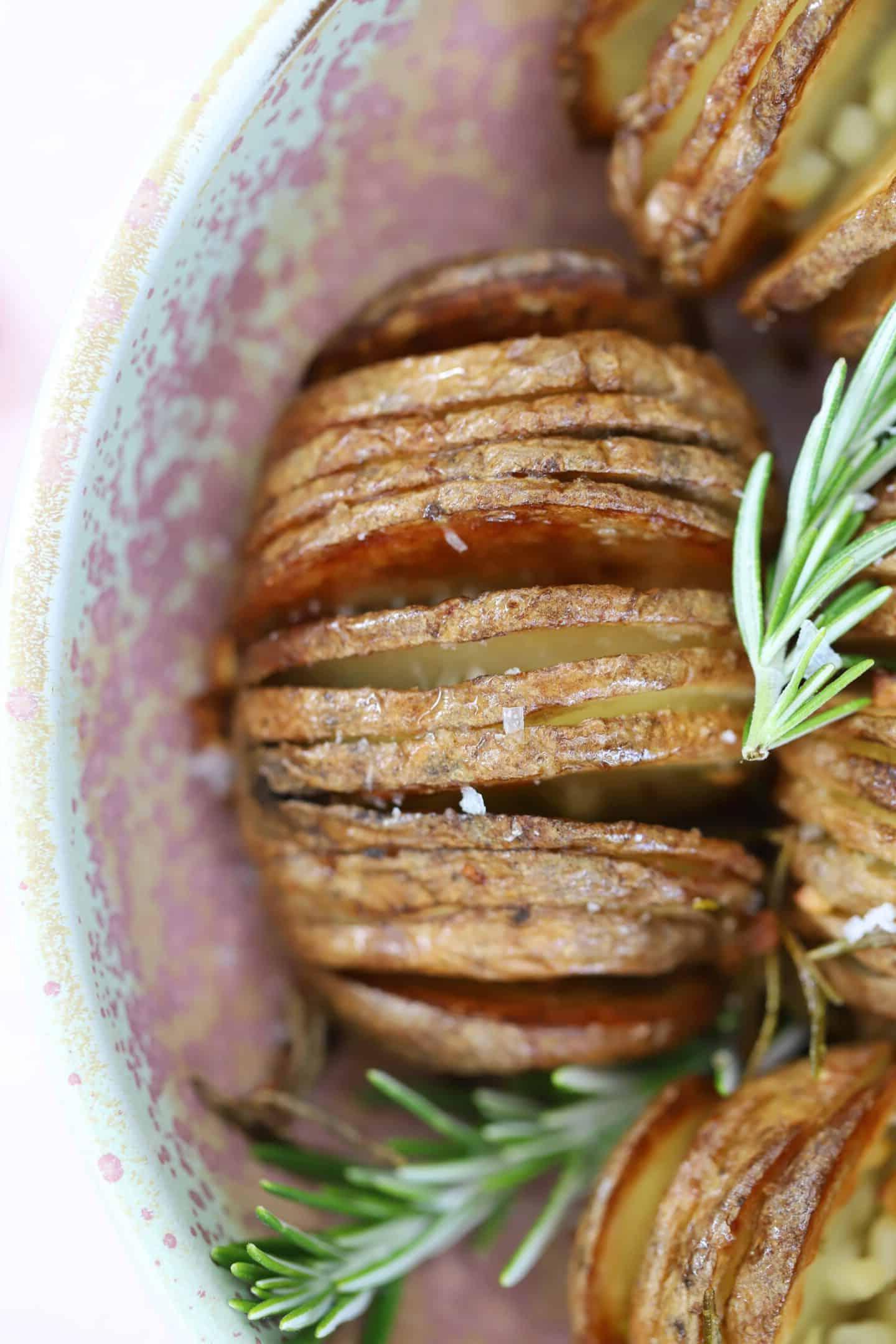Patate Hasselback in friggitrice ad aria 3 Una ciotola di patate hasselback cotte in friggitrice ad aria con rametti di rosmarino.
