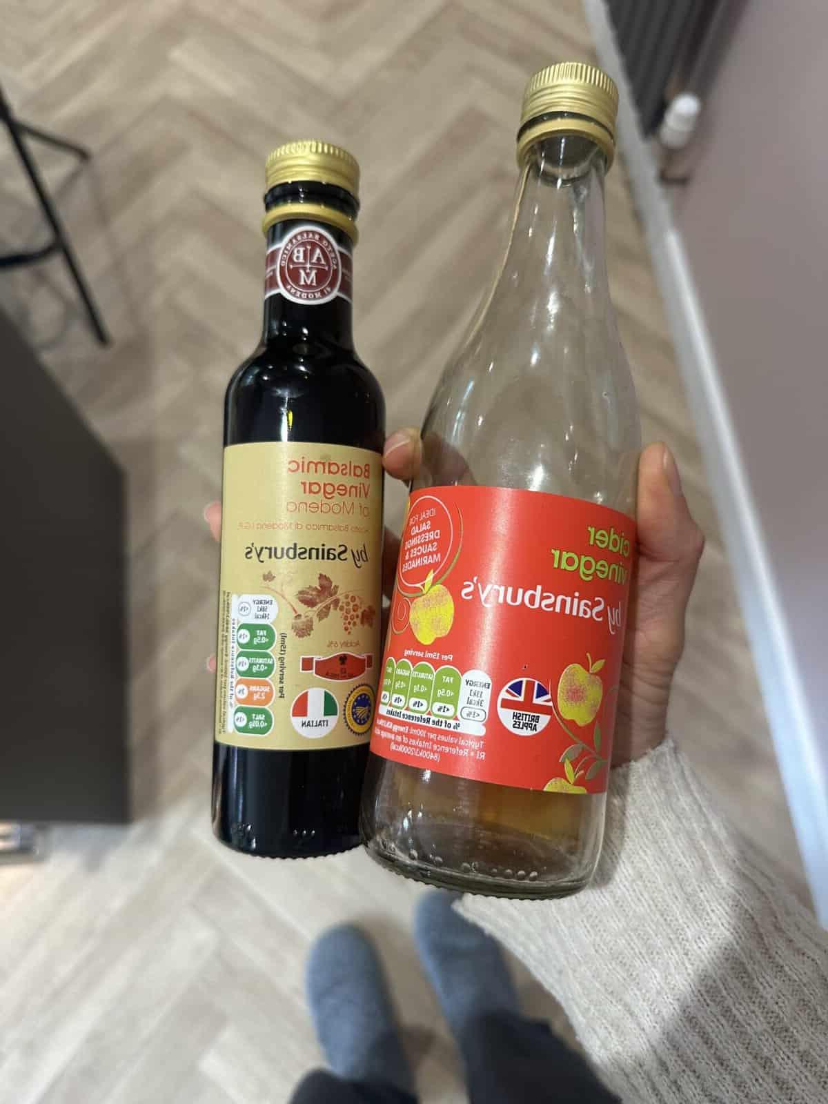 L'aceto è senza glutine? 4 Una mano che tiene bottiglie di aceto di mele e aceto balsamico, simboli di opzioni sicure e deliziose.