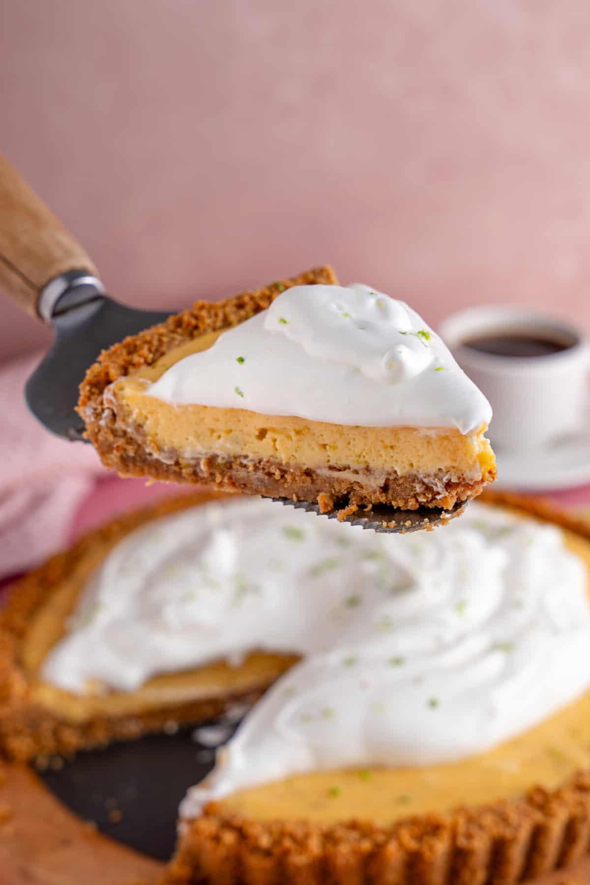 Torta al Lime Senza Glutine 5 Una fetta di torta Key Lime senza glutine con il resto della torta su un tagliere dietro.