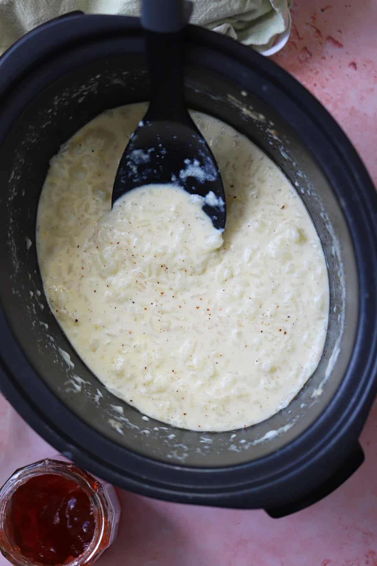 Budino di riso in una slow cooker con un cucchiaio nero per servire.