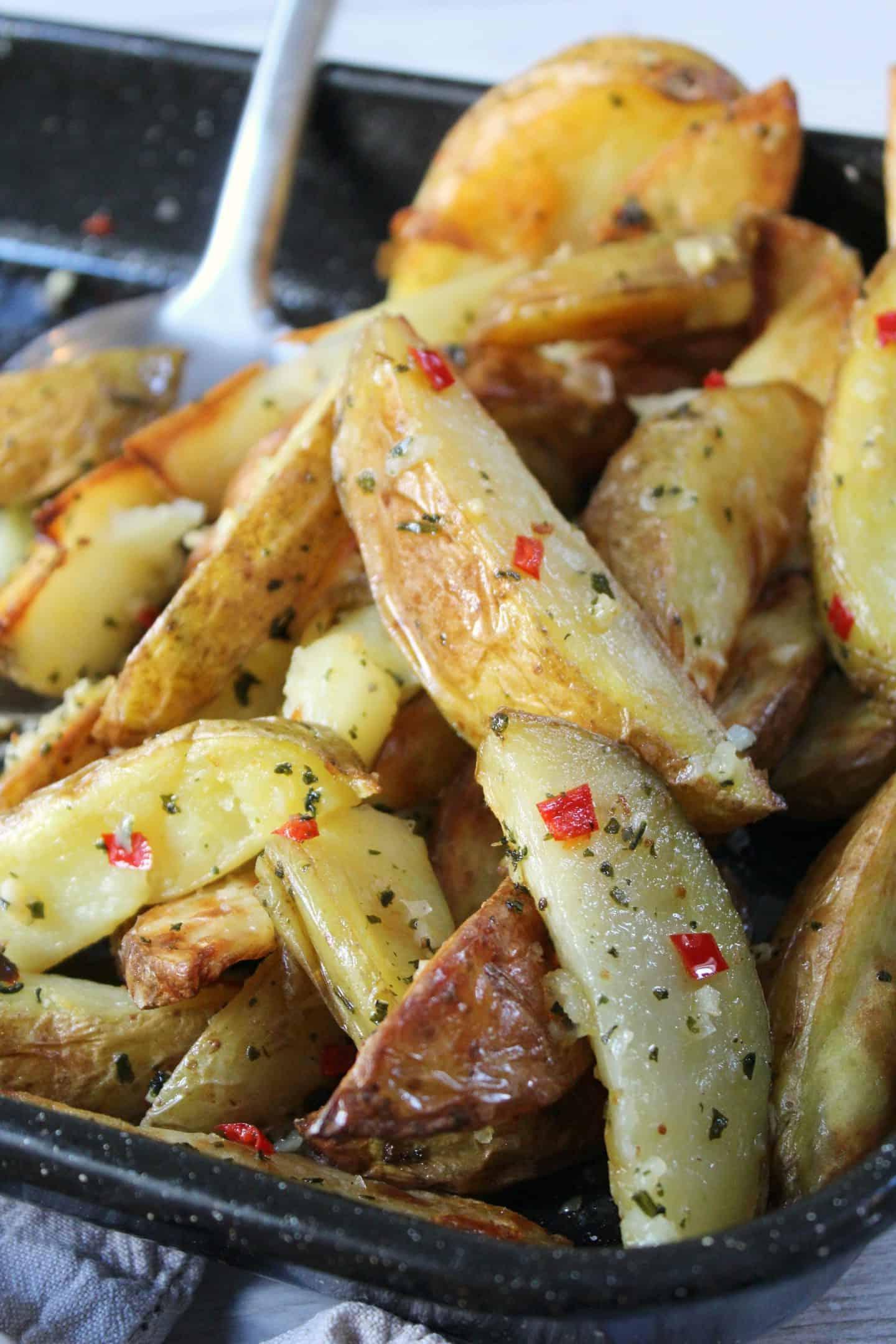 Patate a spicchi senza glutine 8 Spicchi di patate senza glutine con aglio e peperoncino in una teglia da forno.