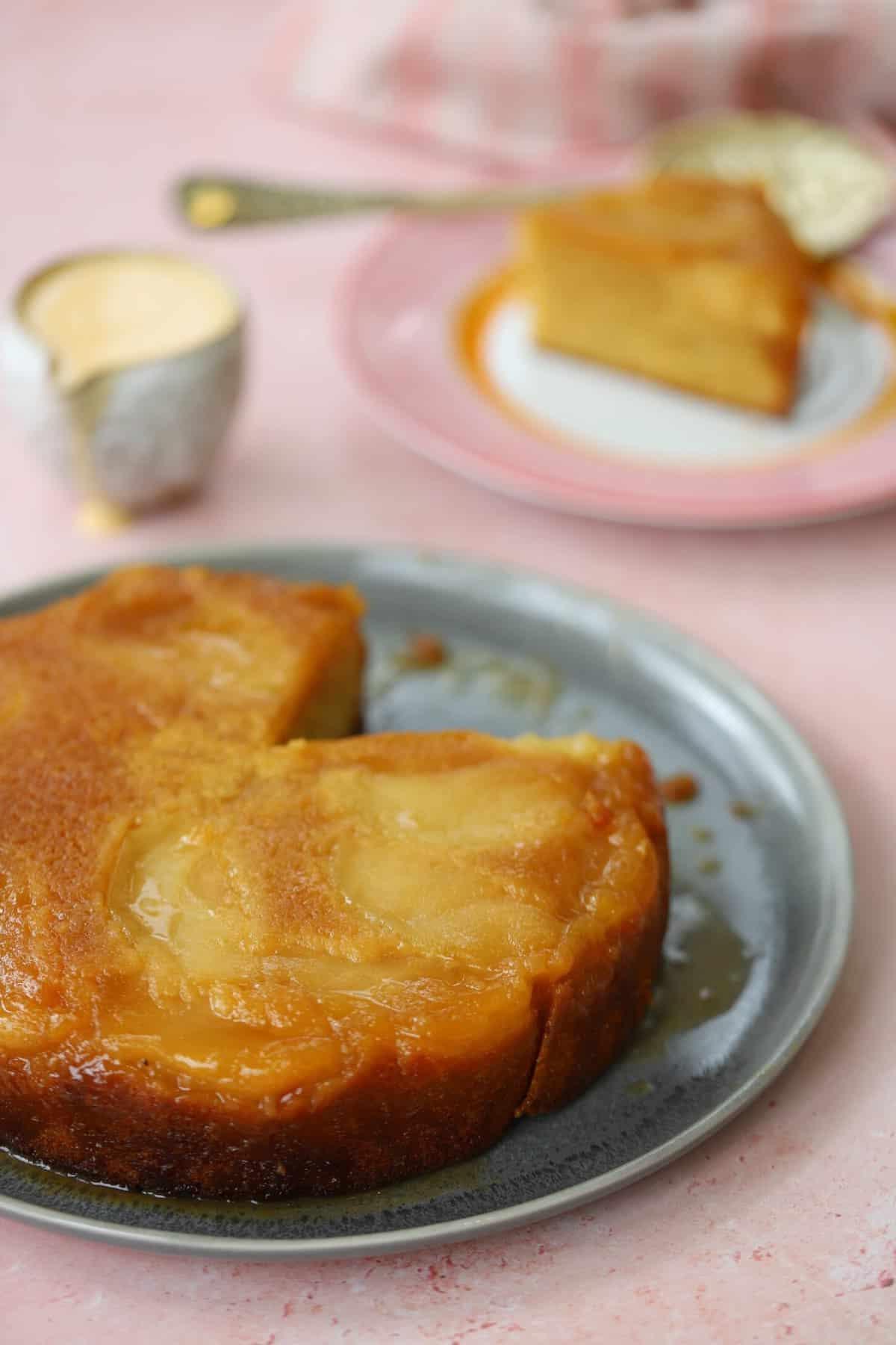Torta di Mele Rovesciata 9 Una torta di mele rovesciata su un piatto con un cuneo tagliato e una brocca di crema inglese sullo sfondo.