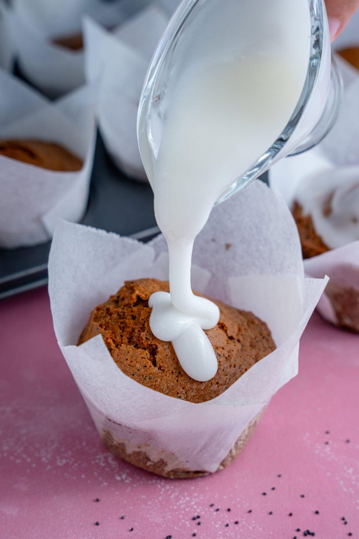 Glassa versata su un muffin senza glutine al limone e semi di papavero.