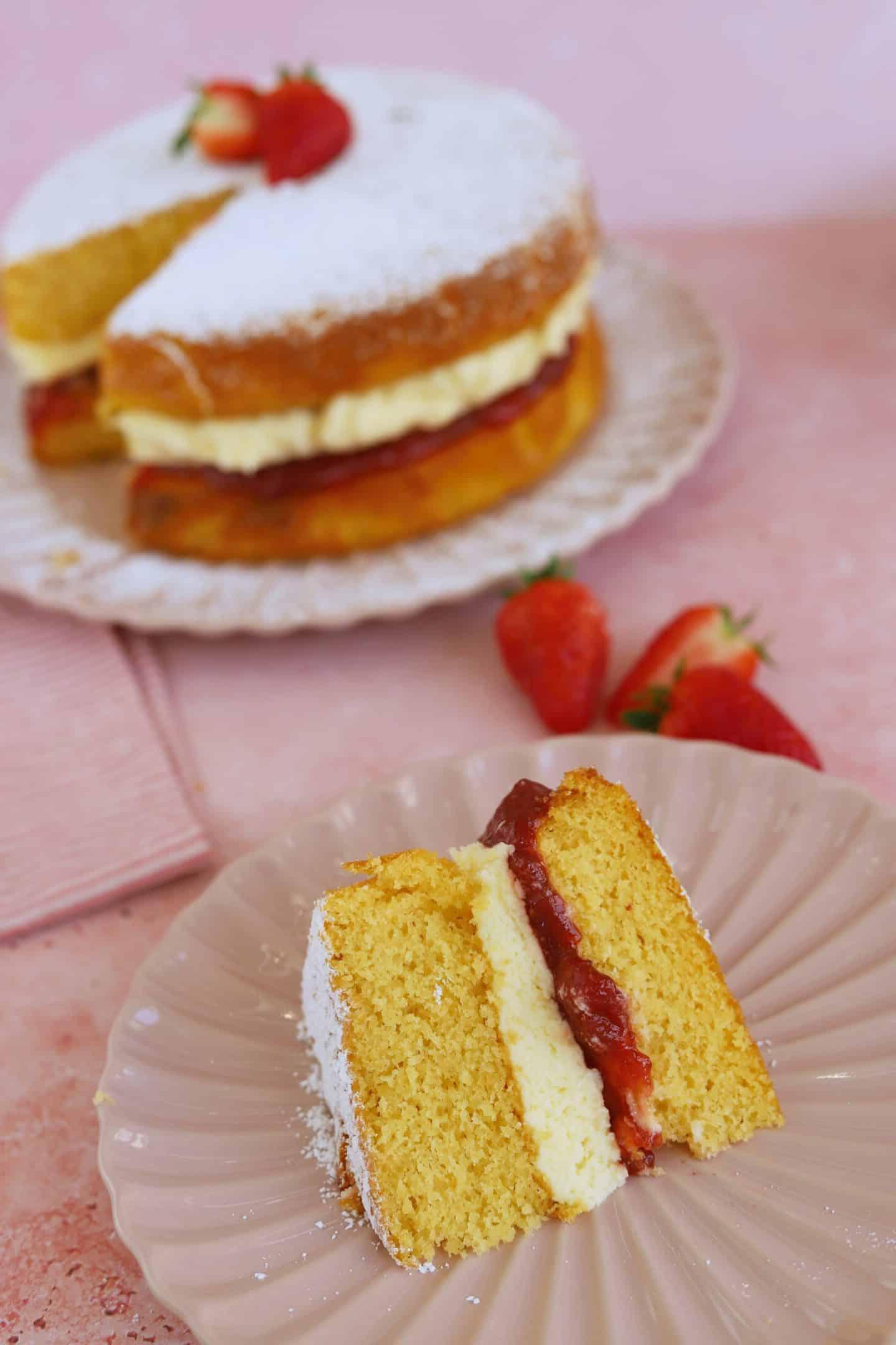 Torta Victoria Senza Glutine 10 Una singola fetta di Torta Victoria senza glutine, riccamente farcita con burrocrema e marmellata, presentata su un piatto con zucchero a velo, evidenziando la sua consistenza umida e i colori vivaci.