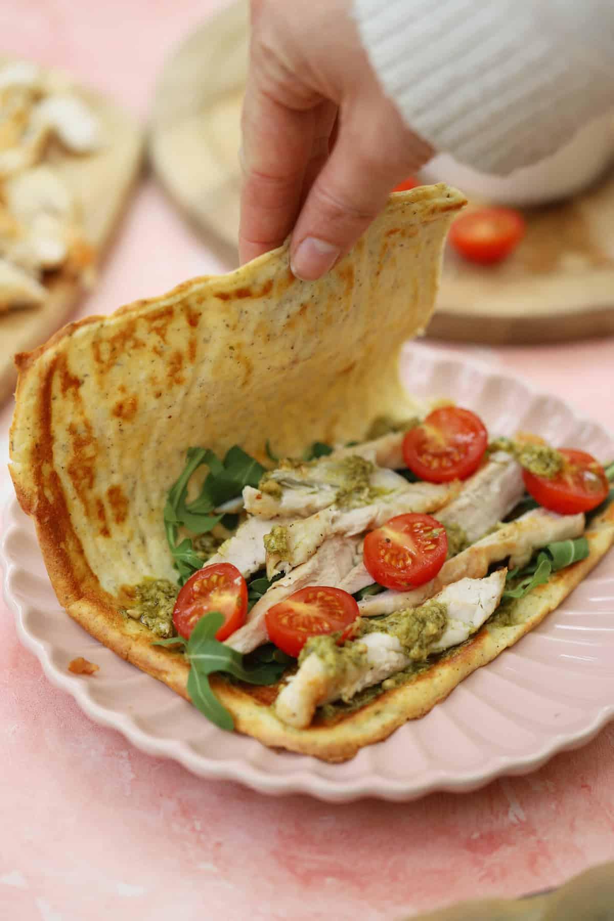 Focaccia con Ricotta 2 Una mano piega una piadina di fiocchi di latte ripiena di pollo, pomodoro e rucola.