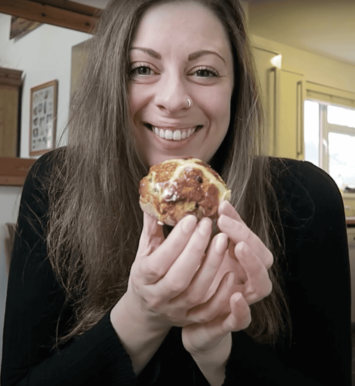 L'autrice Sarah Howells mostra un Hot Cross Bun senza glutine, sorridendo.
