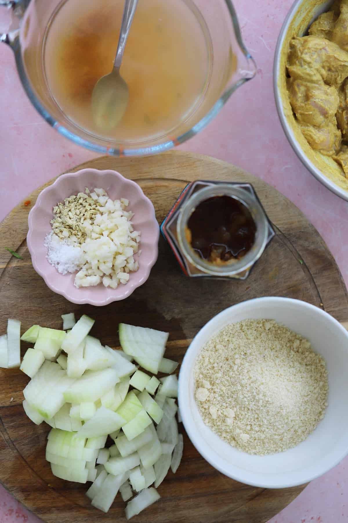 Korma di Pollo a Cottura Lenta 4 Gli ingredienti per un korma di pollo in slow cooker su una superficie di lavoro rosa.
