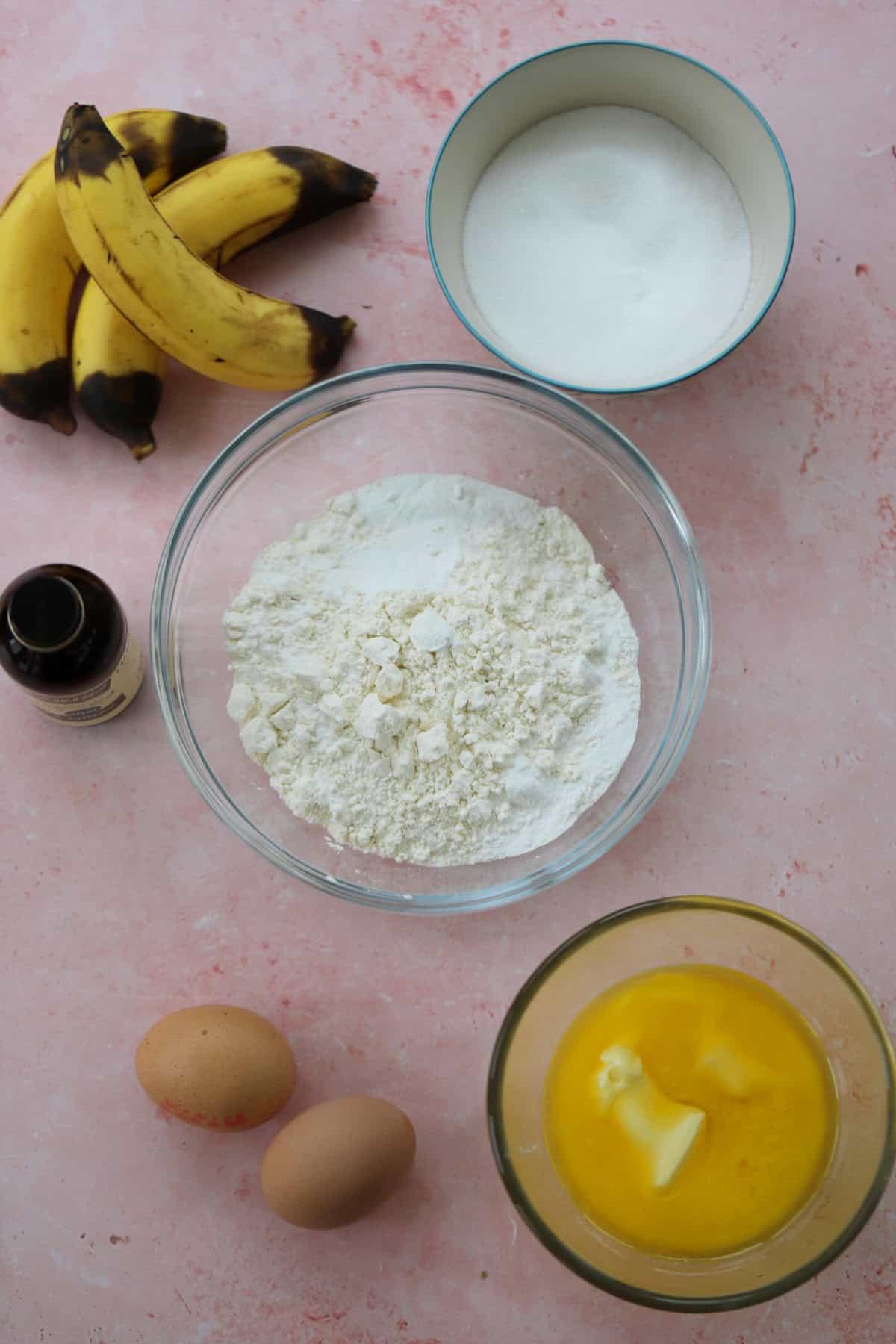 Banana Bread Senza Glutine 4 Gli ingredienti per il banana bread senza glutine disposti su uno sfondo rosa.