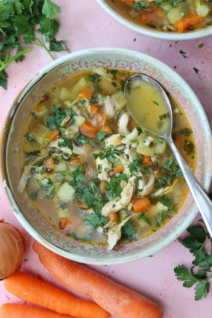 Zuppa di Pollo Senza Glutine 7 Una ciotola di zuppa di pollo senza glutine con un cucchiaio su uno sfondo rosa.