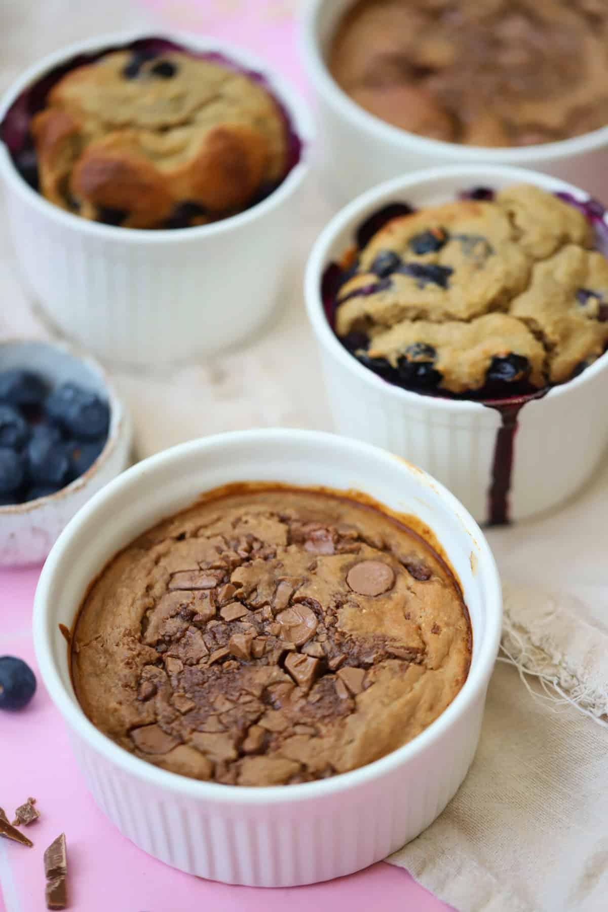 Avena al Forno 7 Una selezione di piccole ciotole bianche contenenti avena al forno al cioccolato o avena al forno ai mirtilli.