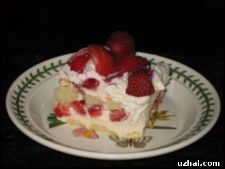 A layered dessert in a glass dish, showing ladyfingers, white chocolate cream, and sliced strawberries, topped with whipped cream and more strawberries.