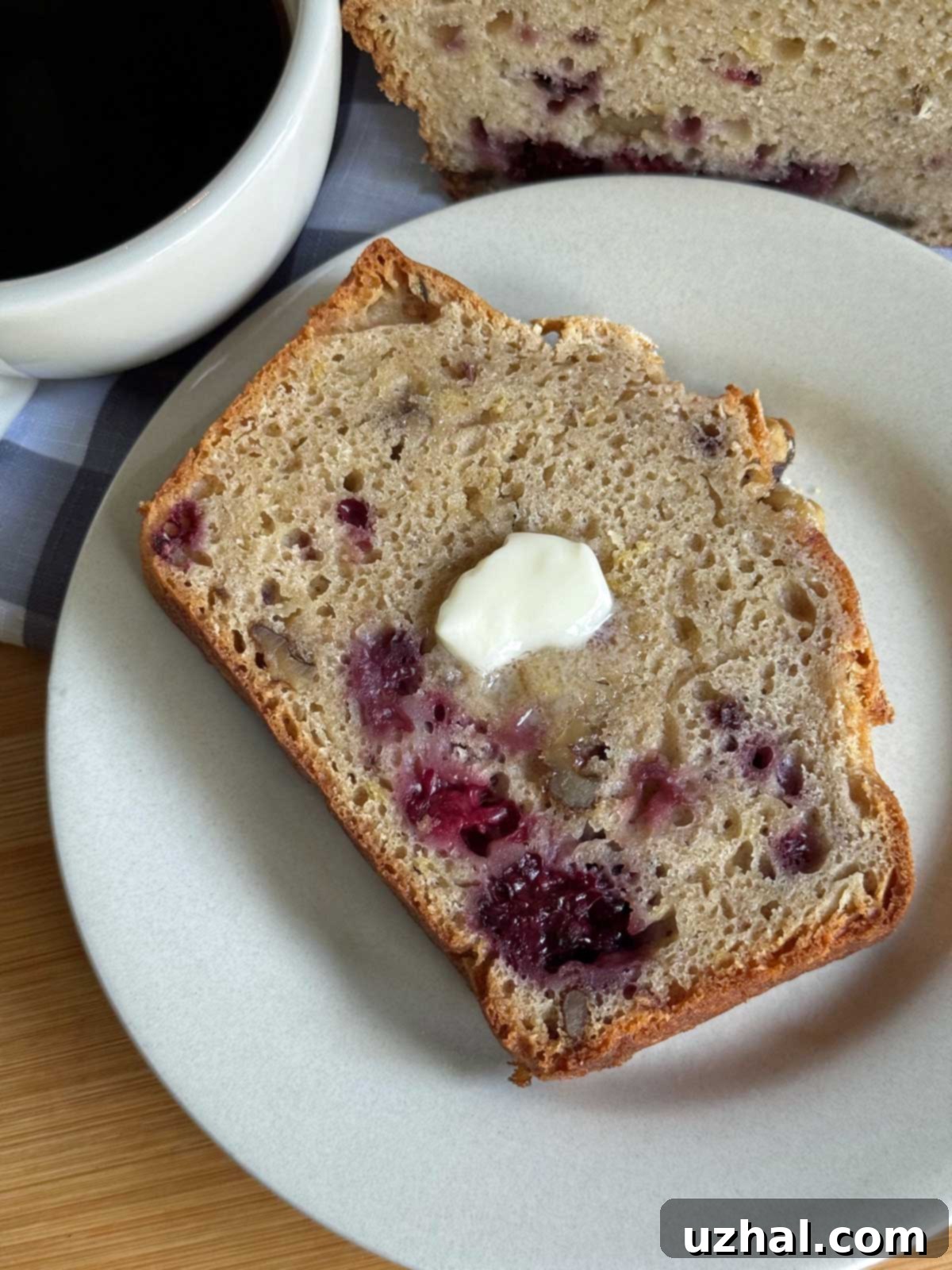 A slice of lightly toasted blackberry quick bread on a plate with butter and coffee, showcasing its moist texture and berry swirls.