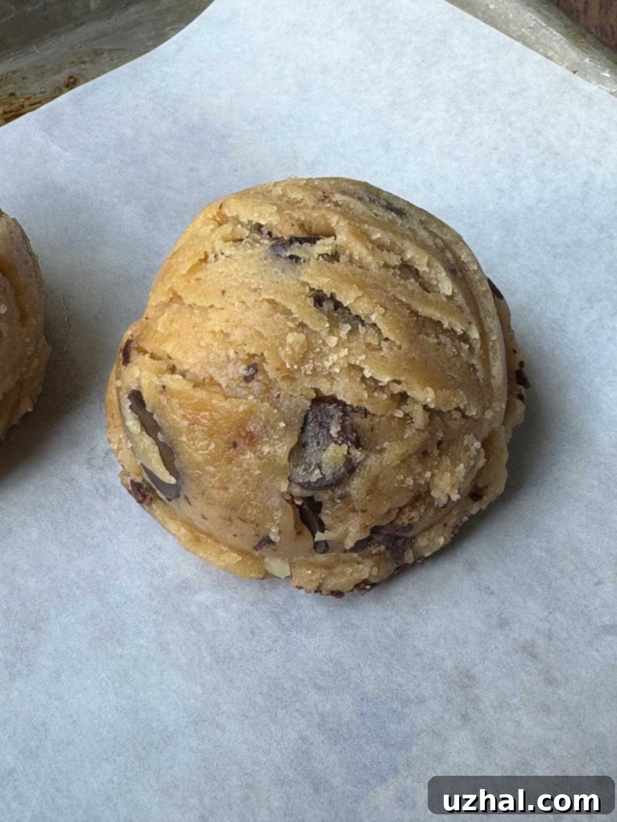 A scoop of dairy-free chocolate chip cookie dough sits on parchment paper, showcasing the generous amount of chocolate chips.