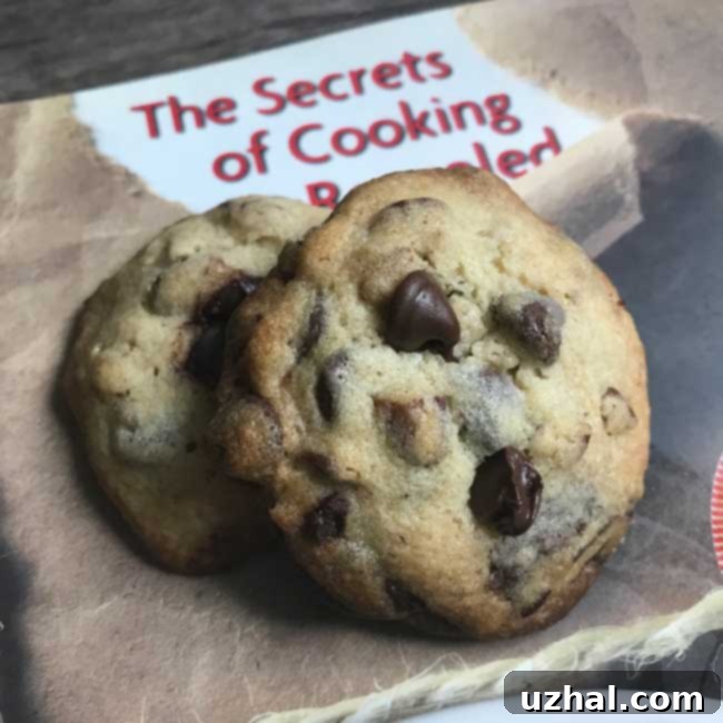 Close-up of golden-brown 'In Between' Chocolate Chip Cookies with melted chocolate chips, resting on a baking sheet, reflecting perfect texture.