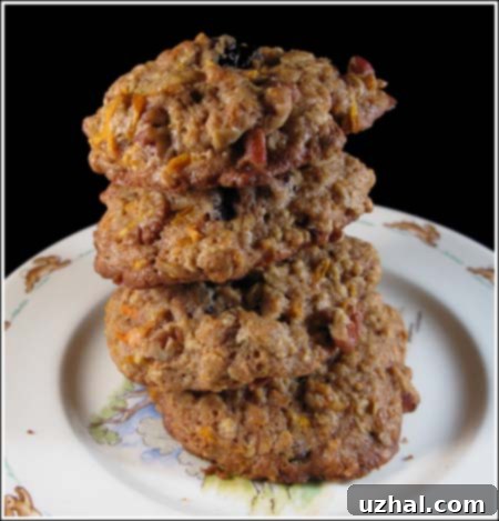 A stack of freshly baked, chewy oatmeal carrot cookies with visible oats, shredded carrots, raisins, and pecans, ready to be enjoyed.