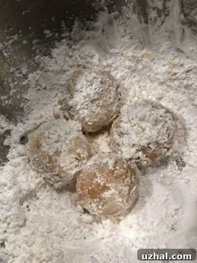 Hot Chai Spiced Almond Cookies being rolled in a bowl of powdered sugar, showing the first dusting process.