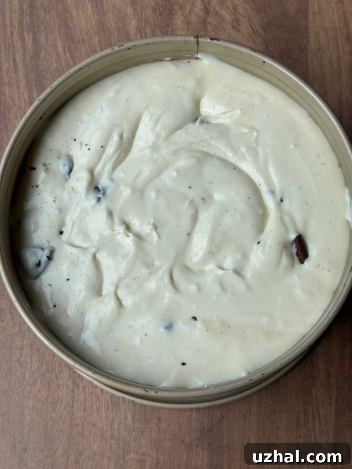 An unbaked Oreo cheesecake mixture spread evenly over the crust in a 7-inch round springform pan, ready for the oven.