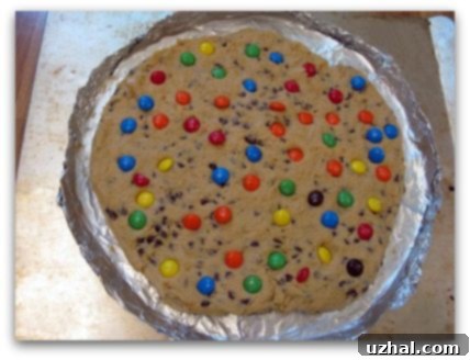 Unbaked giant chocolate chip cookie cake dough in a 14-inch pizza pan, ready for M&M's and the oven.