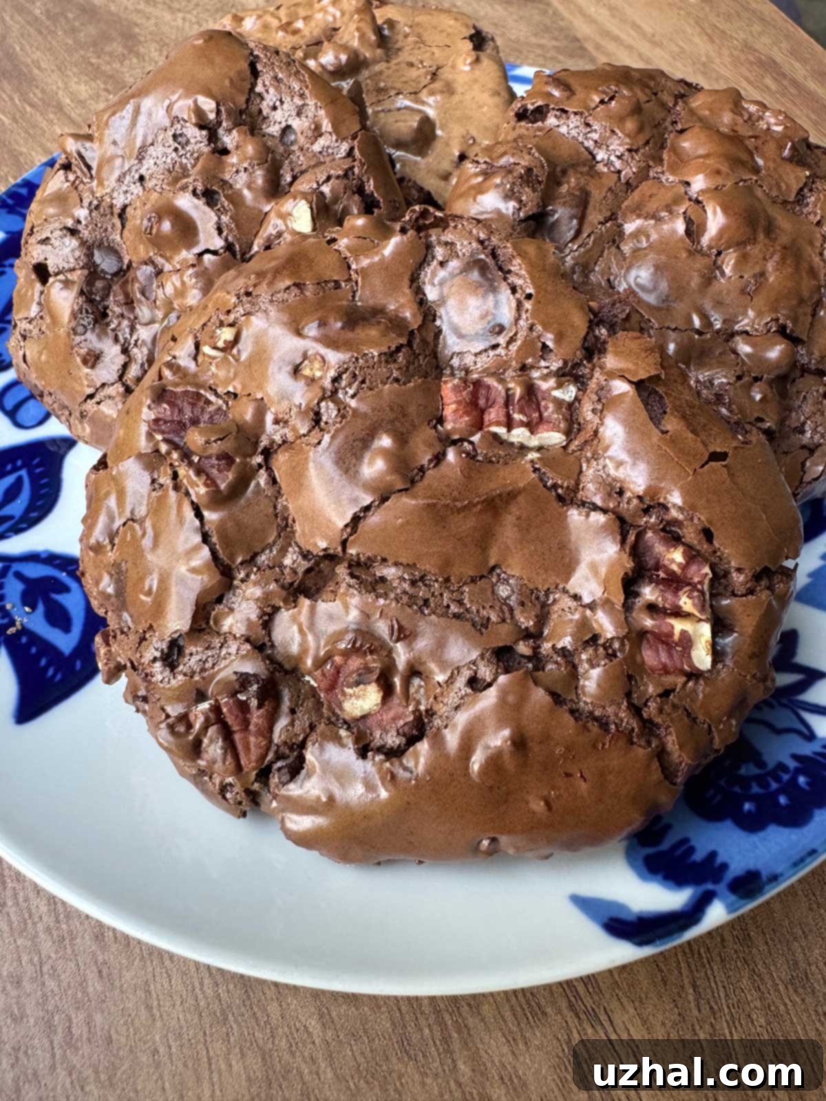 A tray of freshly baked chewy pecan chocolate cookies with distinct crackled tops, made with egg whites and powdered sugar, cooling on parchment paper.