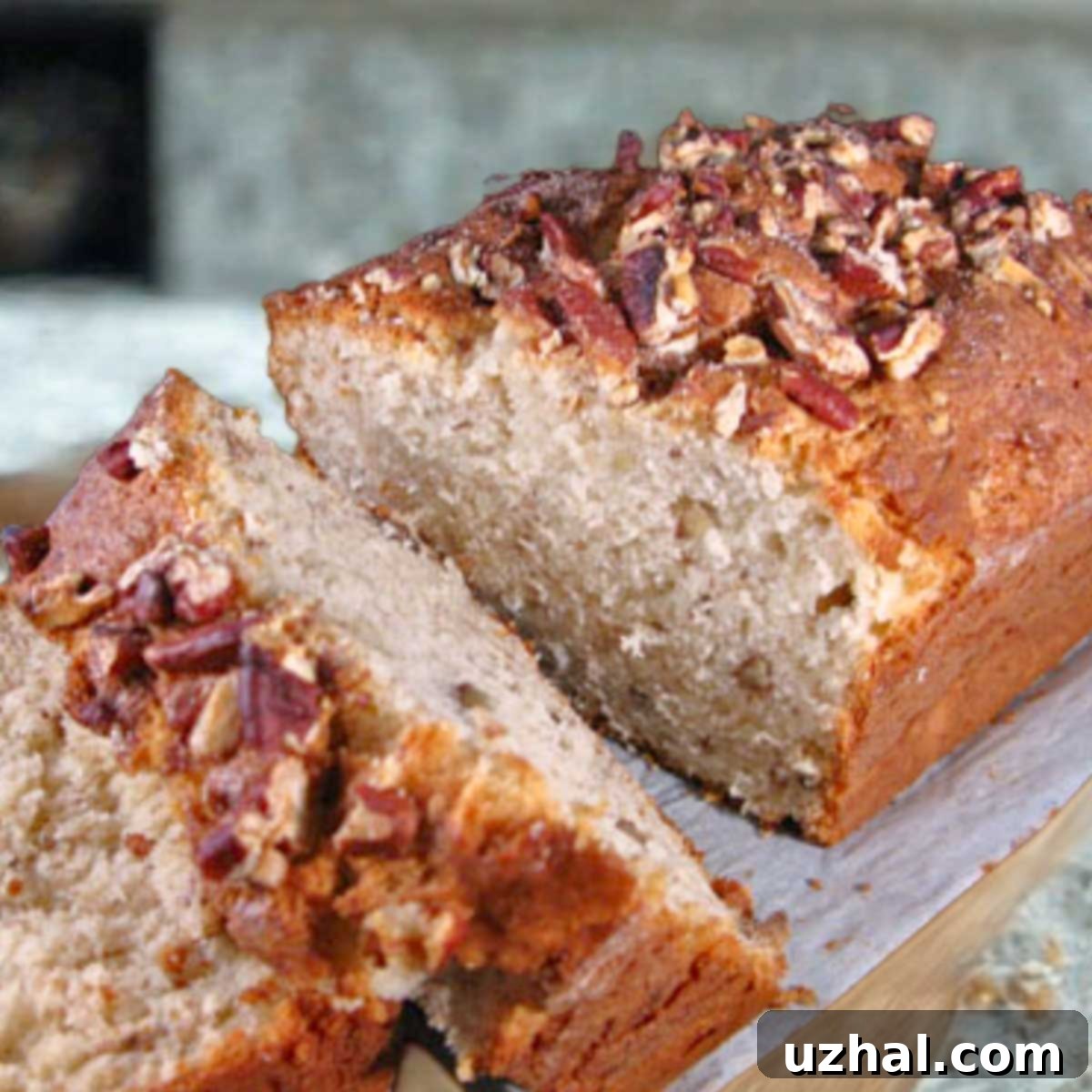 A slice of moist Cream Cheese Banana Bread showing its light texture and specks of nuts. The loaf has a golden-brown crust and a dusting of cinnamon sugar.