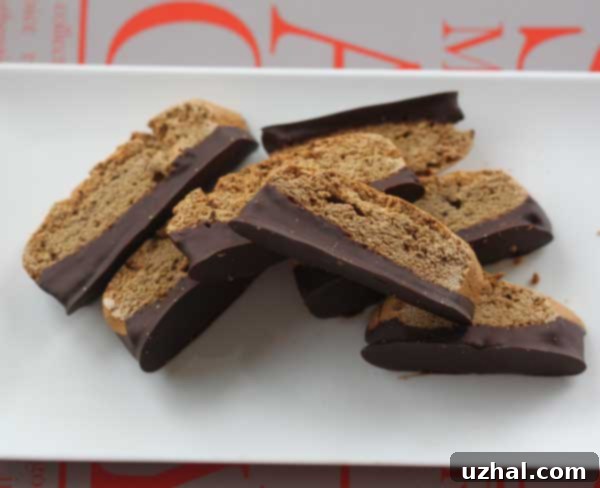 Golden brown cassava flour biscotti, with one end dipped in melted chocolate, resting on a white surface.