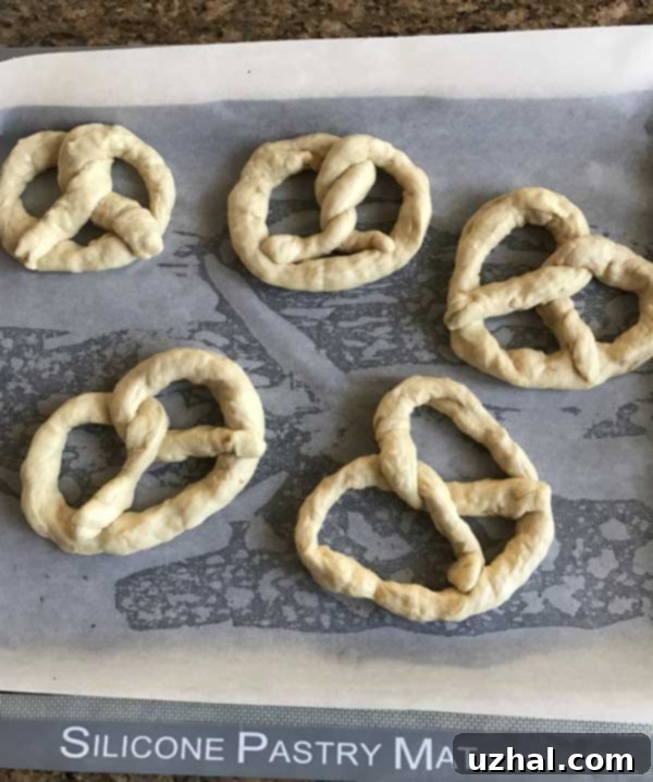 Close-up of homemade soft pumpernickel pretzels on a baking sheet, showing their coarse salt topping and perfect browning.