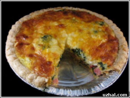 A golden-brown quiche sliced, revealing layers of ham, cheddar, Gouda, and spinach, presented on a white plate.