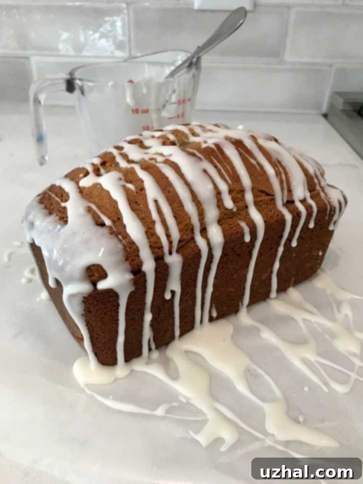 A freshly baked loaf of apple bread with a delicate, opaque white icing generously drizzled over the top, ready to be served.