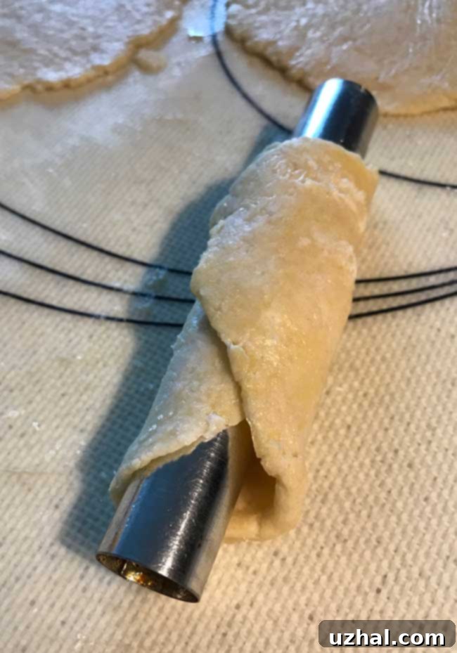 Cannoli form with homemade cannoli dough wrapped around it, ready for frying.