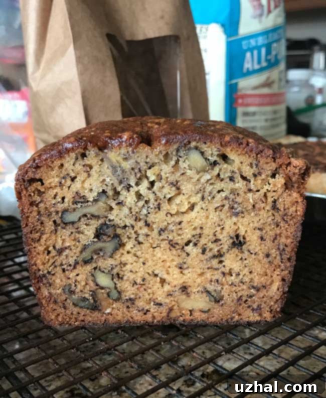 Moist, golden-brown slice of banana bread with walnuts, made from two bananas, resting on a cutting board.