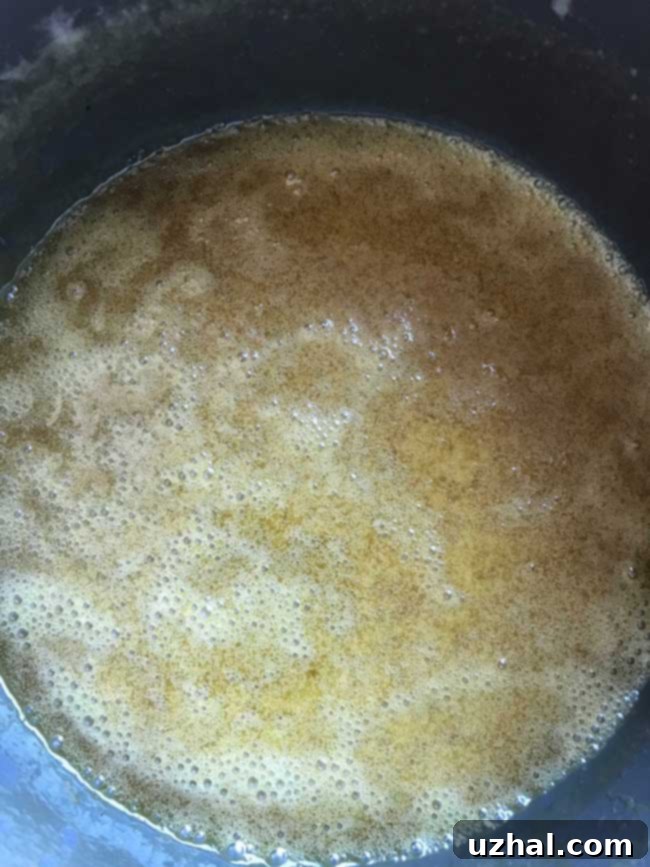 Close-up of buttermilk glaze being prepared in a saucepan, showing its rich, golden-brown color and frothy texture, destined for a Southern Living carrot cake.
