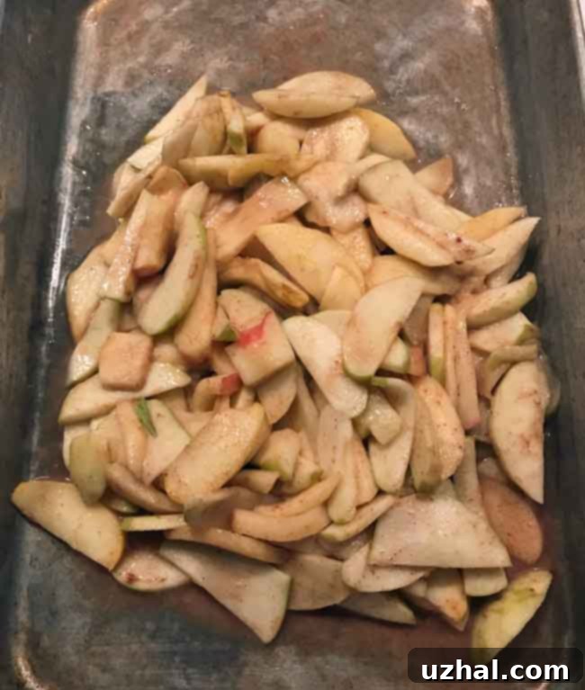 Sliced apples being broiled in a roasting pan, softening and releasing their natural juices for the pie filling