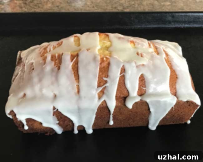 A fully baked lemon loaf cake with a generous drizzle of white lemon icing on top, garnished with fresh lemon slices.