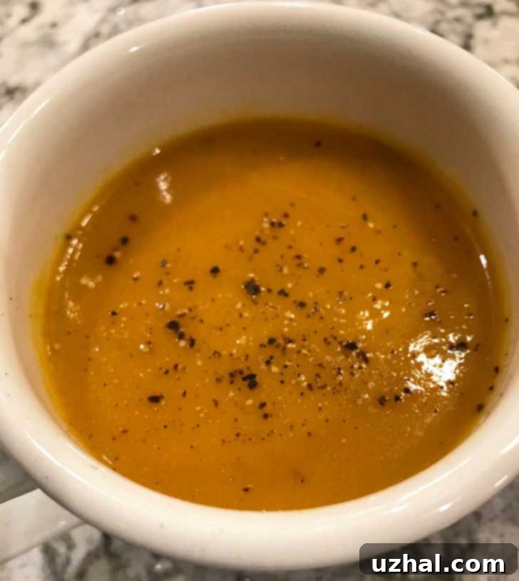 A vibrant bowl of Carrot Cardamom Soup, garnished with a sprig of fresh herbs, presented on a rustic wooden surface.